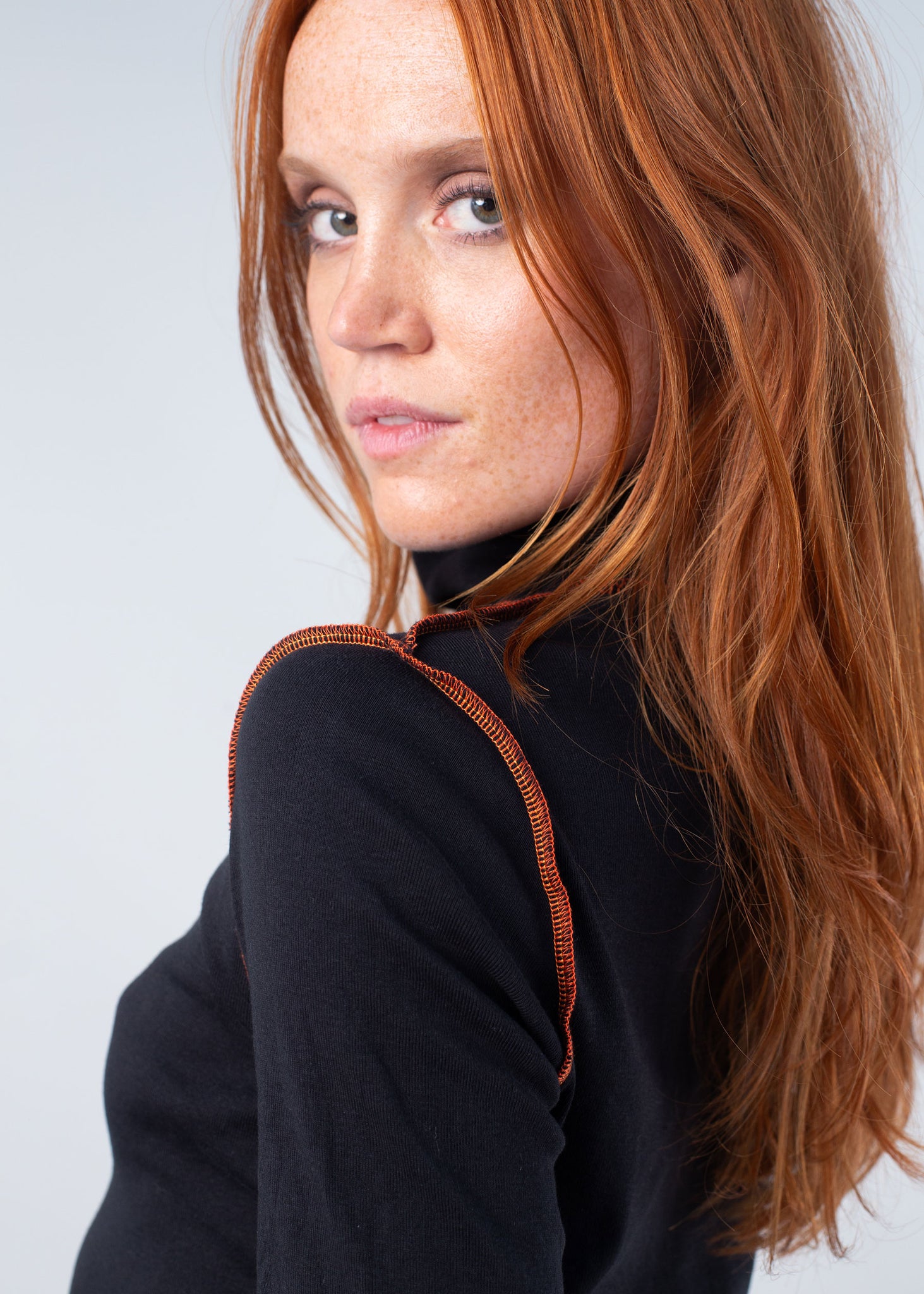 woman with red hair wearing the organic turtleneck reversed in black with orange pop color topstitching