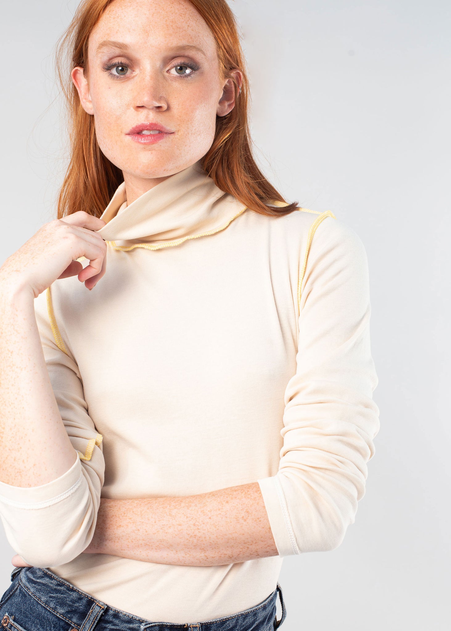 A woman with red hear wearing the undyed turtleneck inside out with pop color stitching